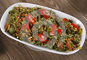 Tabbouleh salad with bulgur, tomatoes, parsley and green onion in plate on wooden table.