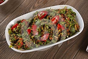Tabbouleh salad with bulgur, tomatoes, parsley and green onion in plate on wooden table