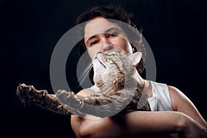 Tabby cat stretches in her arms near a beautiful girl on black background