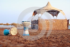 Tabla or darbuka, egyptian music instrument, sandy beach background with summerhouse