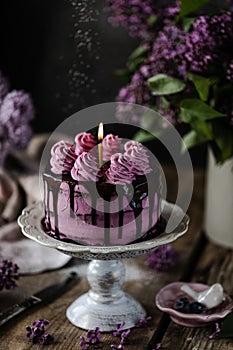 On the table is a beautiful chocolate cake and a bouquet of lilacs. dark