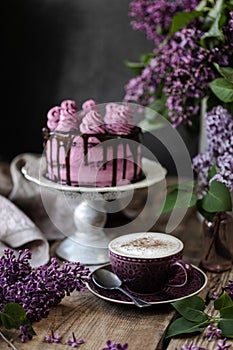 On the table is a beautiful chocolate cake and a bouquet of lilacs. dark