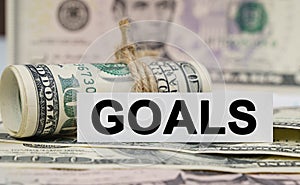 On the table are bills, a bundle of dollars and a sign on which it is written - GOALS