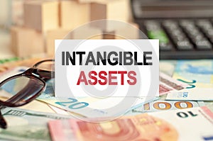 On the table are bills, a bundle of dollars and a sign on which it is written - INTANGIBLE ASSETS. Finance and economics concept