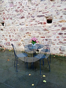 Table with blue chairs and a flower pot with flowers on the background of a brick wall