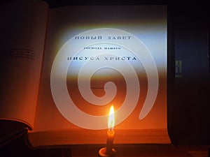 On the table is a book on which the inscription "Holy Bible" in Russian is illuminated. A candle is burning next to it