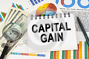 On the table are business charts, dollars and a notepad with the inscription - capital gain