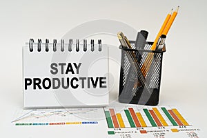 On the table are business charts, office supplies and a notepad with the inscription - stay productive