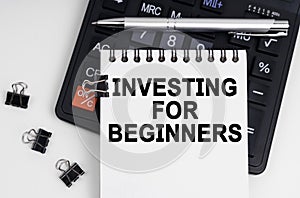 On the table is a calculator, a pen and a notebook with the inscription - INVESTING FOR BEGINNERS