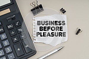 On the table is a calculator, a pen and paper with the inscription - Business Before Pleasure