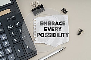 On the table is a calculator, a pen and paper with the inscription - Embrace Every Possibility