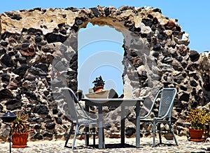 Table and chairs with old stone wall in Santorini