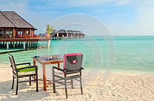 Table and chairs at restaurant at the background of water bungalows, Maldives