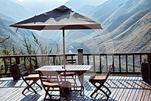 Table and chairs under umbrella on terrace against blue mountain