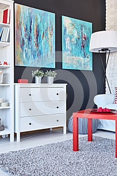 Table, chest of drawers and paintings in a room