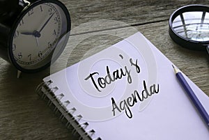 Table clock,magnifying glass,pencil and notebook written with Today's Agenda on wooden background photo