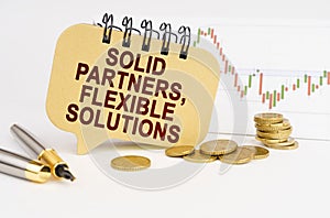 On the table are coins, a pen, a graph and a sign with the inscription - Solid partners, flexible solutions