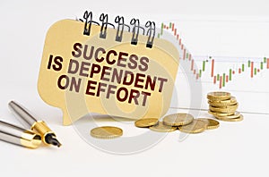 On the table are coins, a pen, a graph and a sign with the inscription - Success is Dependent on Effort