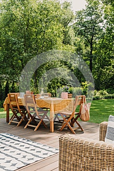 Table covered with orange tablecloth standing on wooden terrace in green garden