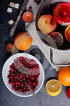 On the table is cranberries, a pan with a mulled wine, an orange and a lemon. View from above.