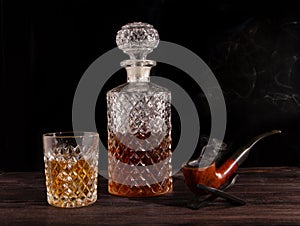 On the table are a decanter and a glass of whiskey and a smoking pipe
