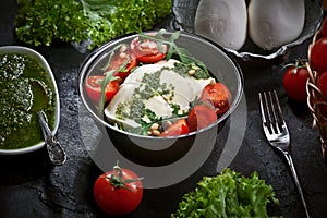 Table decorated with fresh mozzarella salad with lettuce and arugula leaves, pesto sauce, fresh cherry tomatoes and cedar nuts, on