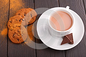On a table, a delicious cocoa in a cup with and a few cookies with chocolate Inside.