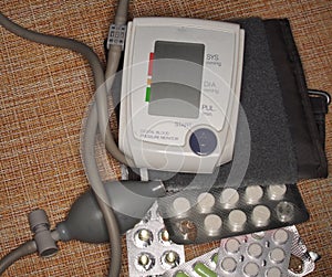 On the table is an electronic blood pressure monitor and medicines in tablets and capsules