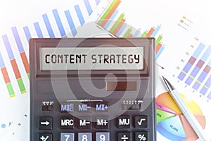 On the table are financial charts and a calculator, on the electronic board of which is written the text - CONTENT STRATEGY