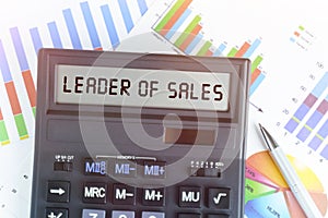 On the table are financial charts and a calculator, on the electronic board of which is written the text - LEADER OF SALES