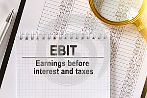 On the table are financial reports, a pen, a magnifying glass and a notebook with the inscription - EBIT