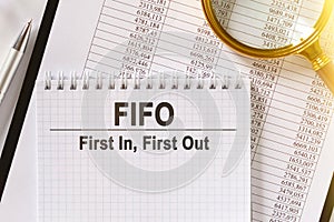 On the table are financial reports, a pen, a magnifying glass and a notebook with the inscription - FIFO
