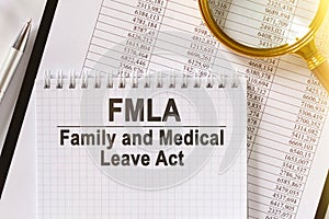 On the table are financial reports, a pen, a magnifying glass and a notebook with the inscription - FMLA photo