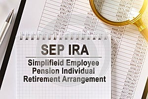 On the table are financial reports, a pen, a magnifying glass and a notebook with the inscription - SEP IRA
