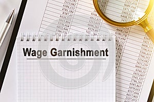 On the table are financial reports, a pen, a magnifying glass and a notebook with the inscription - Wage Garnishment photo