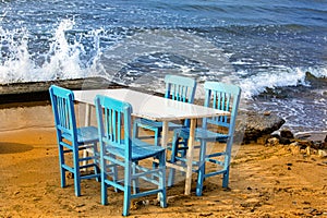 Empty white table with four blue chaires on the beach. Waves crashing onto the shore photo