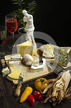 A table full of delicious assorted cheeses with knives, tomatoes,