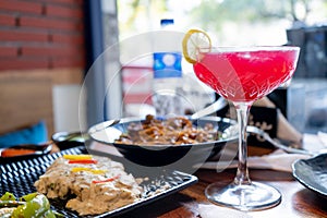 table full of street fast fusion food and tall glass filled with pink red drink of strawberry cherry with lemon showing