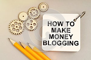 On the table are gears, pencils and a notebook with the inscription - How To Make Money Blogging