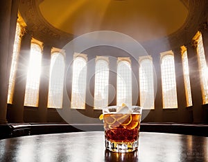 A table with a glass of orange juice on it in front of a large window with sunlight streaming in.