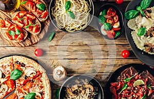 Table of italian meals on plates Pizza, pasta, ravioli, carpaccio, mushroom risotto, caprese salad and tomato bruschetta on rustic