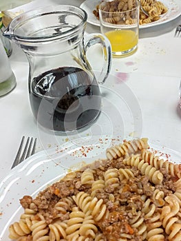 Table laden with 2 pasta dishes, a jug of red wine, a glass with orange juice, all placed on a white tablecloth.