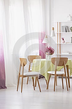 Table with lemon water, fresh heather and green tablecloth in real photo of dining room interior with lamps, window