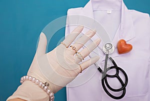 On the table lie the doctor`s clothes and a stethoscope, on top of the doctor`s hand in gloves and wearing jewelry