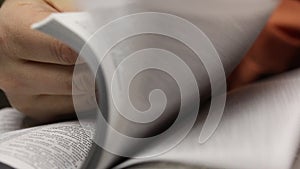 On the table lies an open Bible. A man slowly leafing through pages in search of the right place. Close-up shot