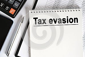 On the table lies a smartphone, a calculator and a notebook with the inscription- Tax evasion