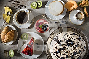 Table with loads of coffee, cakes, cupcakes, cookies, cakepops, desserts, fruits, flowers and croissants.