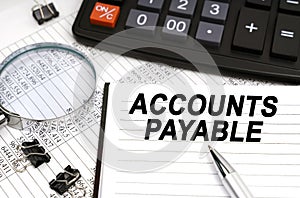 On the table is a magnifying glass, a calculator, a pen and a notebook with the inscription - Accounts Payable