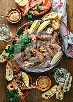 Table with many plates with shrimps, bread, lemons and wine, top view