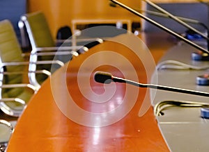 A table microphone in a board room with a wooden table and a row of empty chairs
